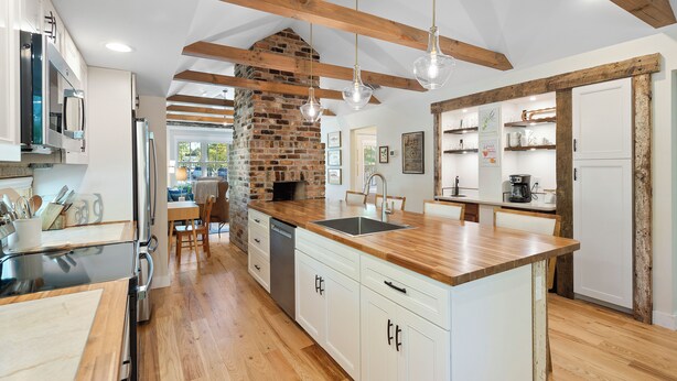 A modern kitchen with wooden beams, a brick fireplace, and a central island. - Cozy Cottage across the street from Carl Sandburg National Park (Flat Rock)