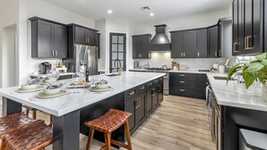 Una cocina moderna con armarios oscuros, una isla de mármol y electrodomésticos de acero inoxidable.