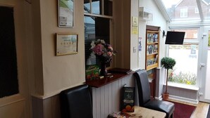 A restaurant interior with a counter, seating area, menu board, and a window with a view of the outside. - Meadows Way Guest House (Uttoxeter)