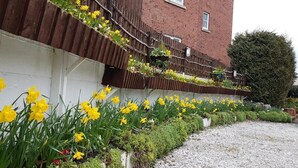 A building with a brick facade and a white wall. There are yellow flowers in front of the building. - Meadows Way Guest House (Uttoxeter)