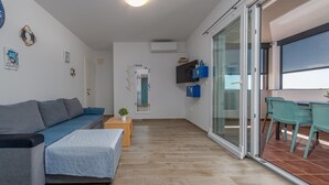 Ett modernt vardagsrum med en soffa, ett litet bord med en växt och en skjutdörr i glas som leder ut till ett utomhusområde med ett bord och stolar.