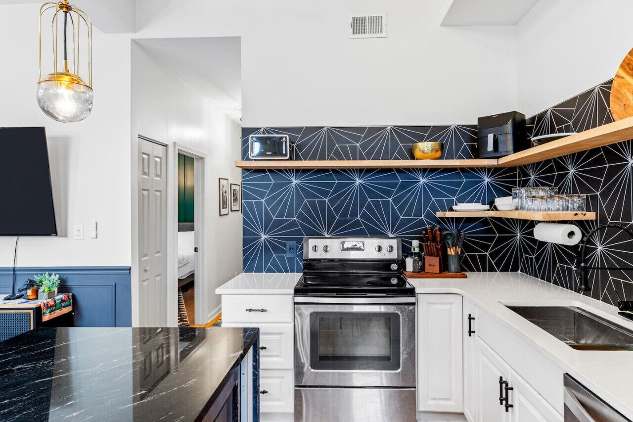 A modern kitchen with a black countertop, stainless steel appliances, and a geometric backsplash.