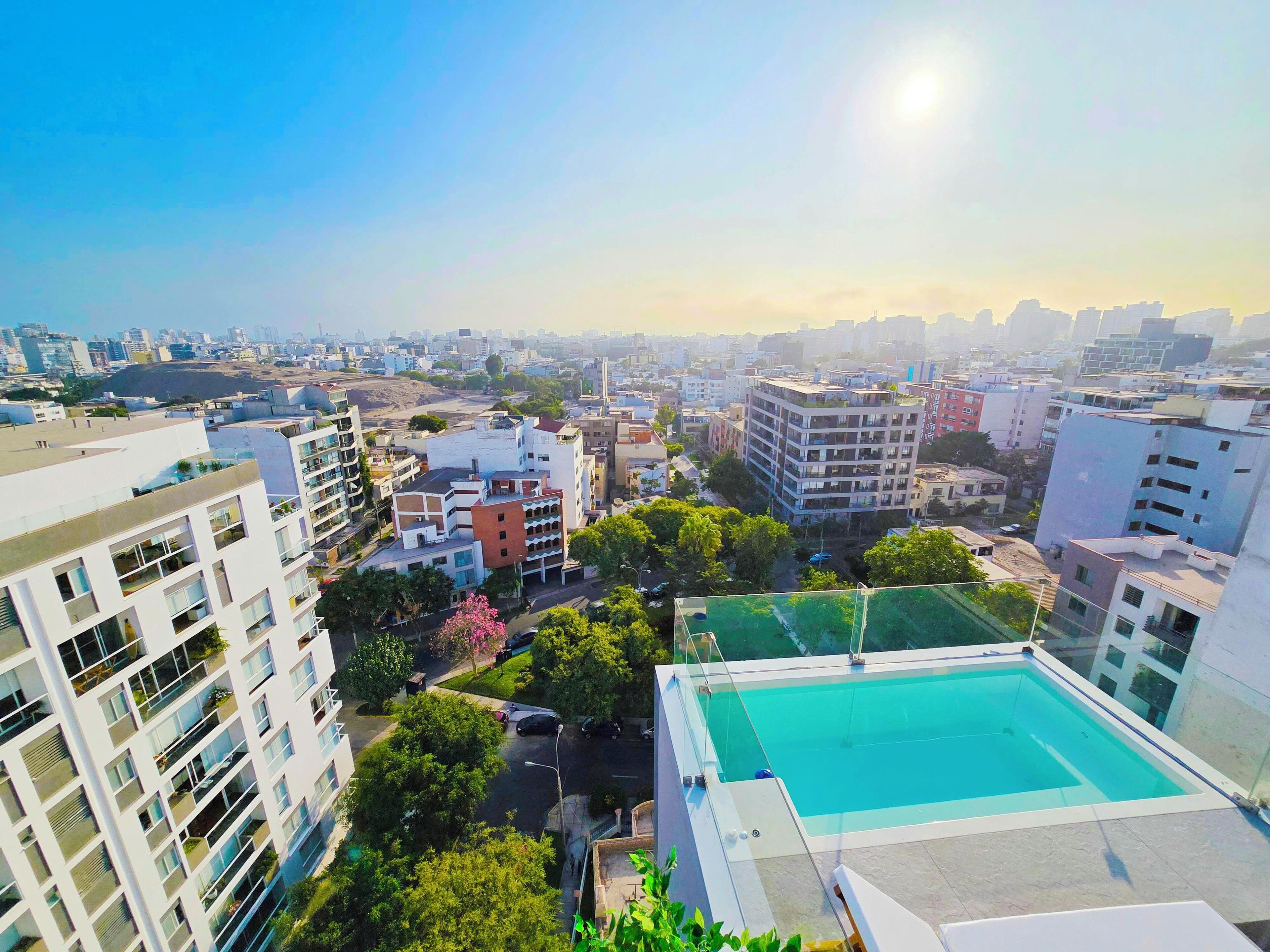 A high-rise building with a rooftop pool, surrounded by other buildings and greenery.
