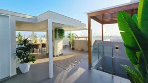 Una terraza moderna en la azotea con zona de comedor, plantas en macetas y vistas del horizonte de la ciudad.