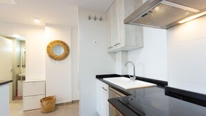A modern kitchen with a black countertop, white sink, and stainless steel appliances. There is a wicker basket on the floor and a decorative mirror on the wall. - 1 bedroom lovely apartment in Denia (Denia)