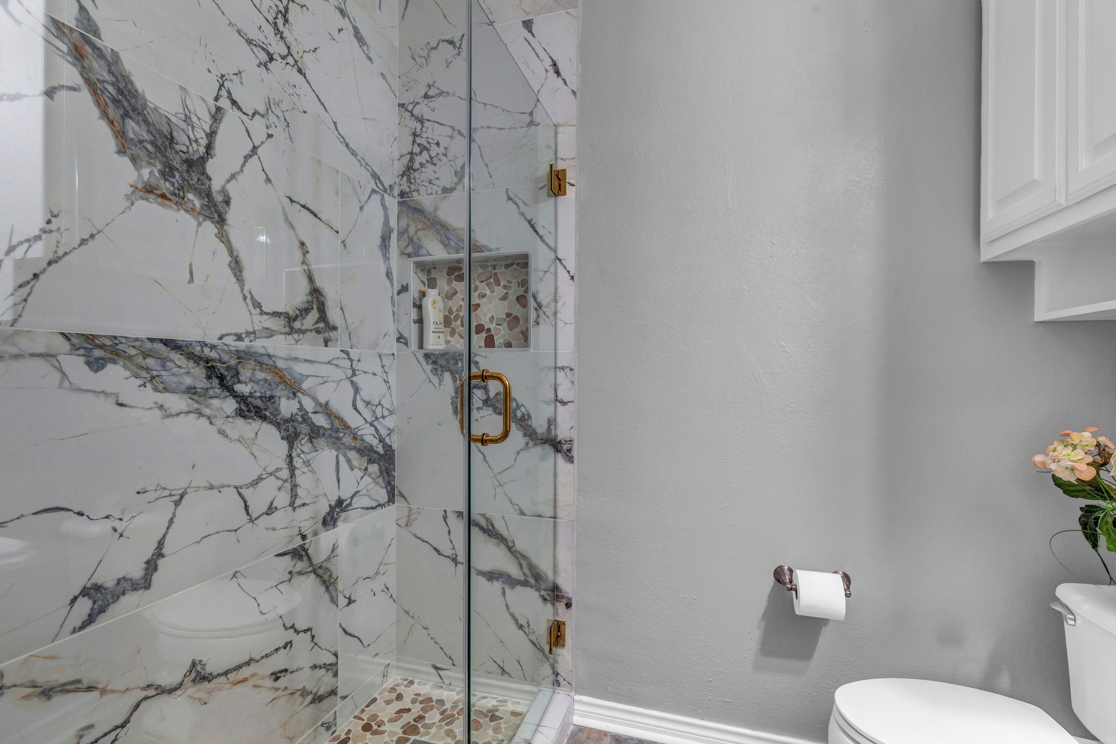 A bathroom with a glass-enclosed shower, marble walls, a toilet, and a sink.
