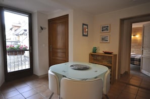 A dining area with a glass table, chairs, a wooden door, and a view of a balcony with flowers. - Apartment 'Appartement Deux Chambres' with Mountain View, Private Terrace and Wi-Fi (Briançon)
