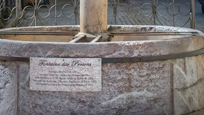 A stone fountain with a plaque, surrounded by a wrought iron fence, in front of a building with arched windows and a sign. - Apartment 'Appartement Deux Chambres' with Mountain View, Private Terrace and Wi-Fi (Briançon)