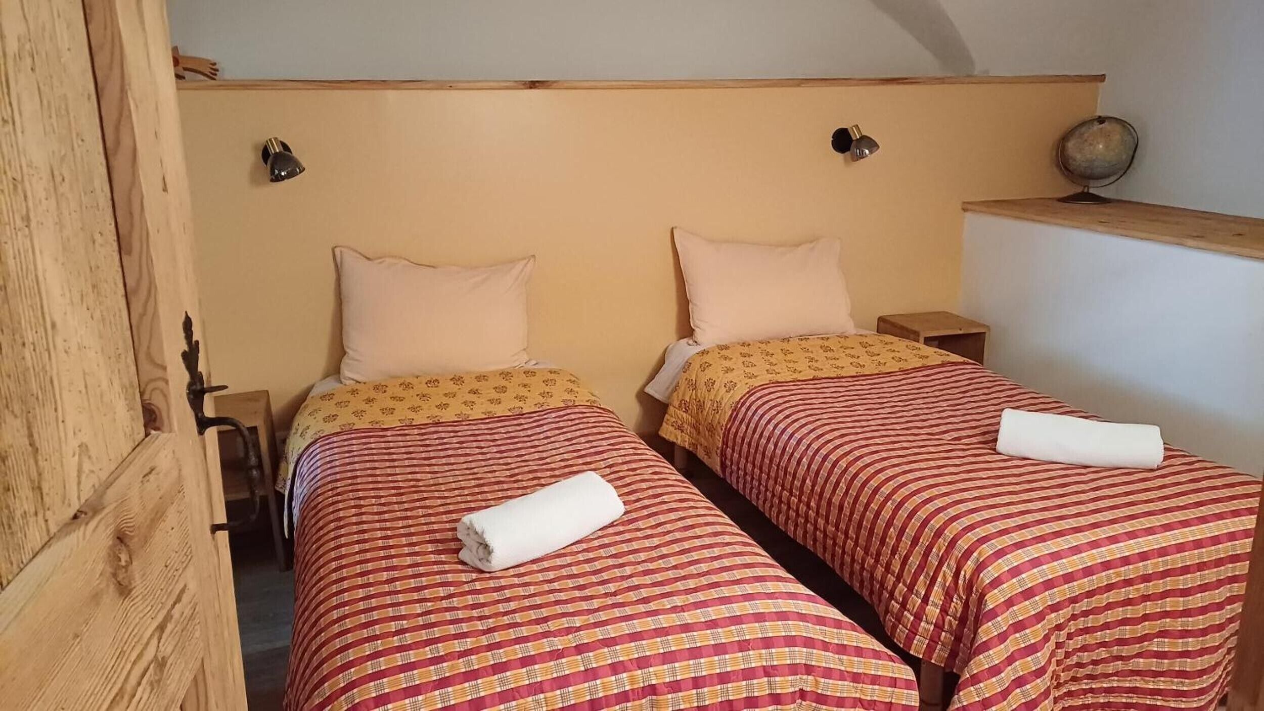 A room with two single beds, each with a patterned bedspread and pillows. There are bedside tables with lamps and a globe on one wall.