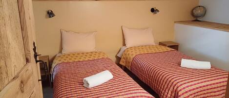 A room with two single beds, each with a patterned bedspread and pillows. There are bedside tables with lamps and a globe on one wall.