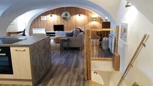A modern kitchen with a dining area, a sofa, and a staircase leading to another level.