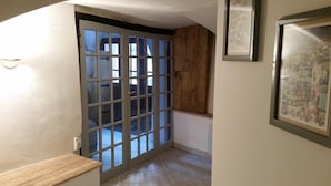A hallway with a wooden door, a framed picture on the wall, and a tiled floor.