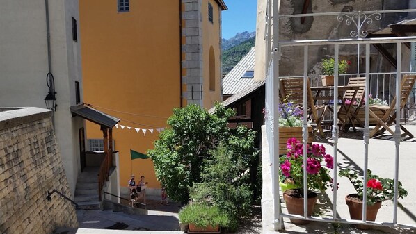A courtyard with a yellow building, a staircase, and a seating area with potted plants.