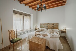 Un dormitorio con una cama grande, una silla, un reposapiés de mimbre, un cabecero de madera y una araña.