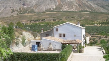 Ein weißes Gebäude mit einem Ziegeldach, einem kleinen Garten und einem Berg im Hintergrund.