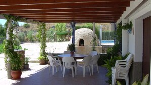 Eine Terrasse im Freien mit einem Steinofen, weißen Plastikstühlen und Blumentöpfen.
