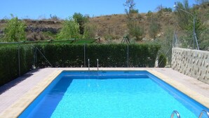 Ein rechteckiger Swimmingpool mit klarem, blauem Wasser, umgeben von einer gefliesten Terrasse und einer Steinmauer.