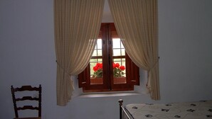 Ein Schlafzimmer mit Fenster, Vorhängen, einem Bett, einem Sessel und einer Chandelüster.