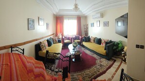 A spacious living room with a yellow sofa, a red patterned rug, and a wooden staircase.