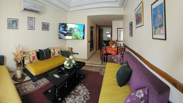 A hallway with a sofa, a table with a vase, and a TV on the wall.