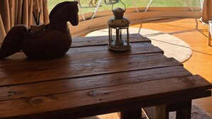 A tent with a view of horses outside, a wooden table with a lantern, and curtains.