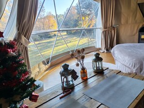 Una habitación acogedora con un ventanal grande, una cama, una mesita con objetos decorativos y un árbol de Navidad.