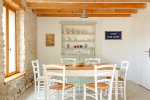 A dining area with a wooden table, white chairs, a green cabinet with dishes, and a sign reading 'Avenue Raoul Dautry'. - Maison "Opaline" with Shared Pool & Spa, Private Terrace, and Wi-Fi (Vergné)