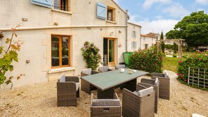 A two-story building with a patio area featuring a table and chairs, surrounded by greenery and a gravel path. - Maison "Opaline" with Shared Pool & Spa, Private Terrace, and Wi-Fi (Vergné)