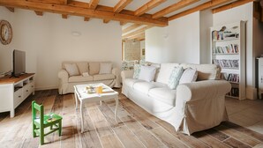 A living room with a white sofa, a green chair, a coffee table, wooden beams on the ceiling, and a bookshelf. - Maison "Opaline" with Shared Pool & Spa, Private Terrace, and Wi-Fi (Vergné)