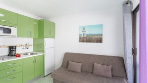 A compact living space with a kitchenette, a sofa, and a painting of a lighthouse.