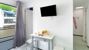 A hotel room with a TV, a small table with breakfast items, a balcony with a view of a building, and a door leading to a bathroom.