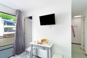 A hotel room with a TV, a small table with breakfast items, a balcony with a view of a building, and a door leading to a bathroom.