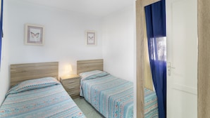 A bedroom with two beds, a nightstand, a door with a curtain, and two framed pictures on the wall.