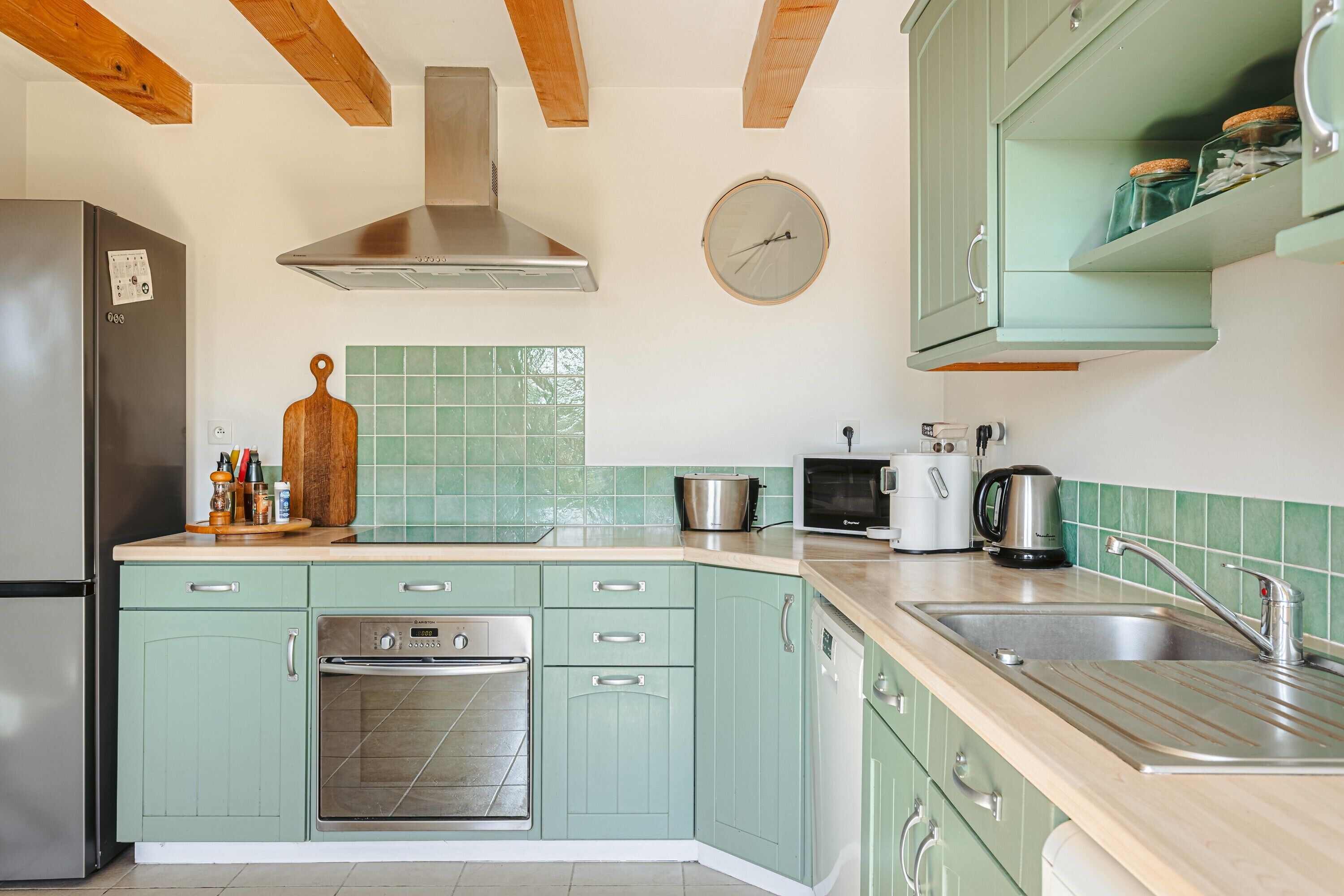 Cucina con mobili verdi, forno in acciaio inossidabile, microonde e lavandino.