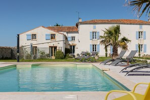 Una piscina con lettini, un'area recintata e un edificio con persiane blu.