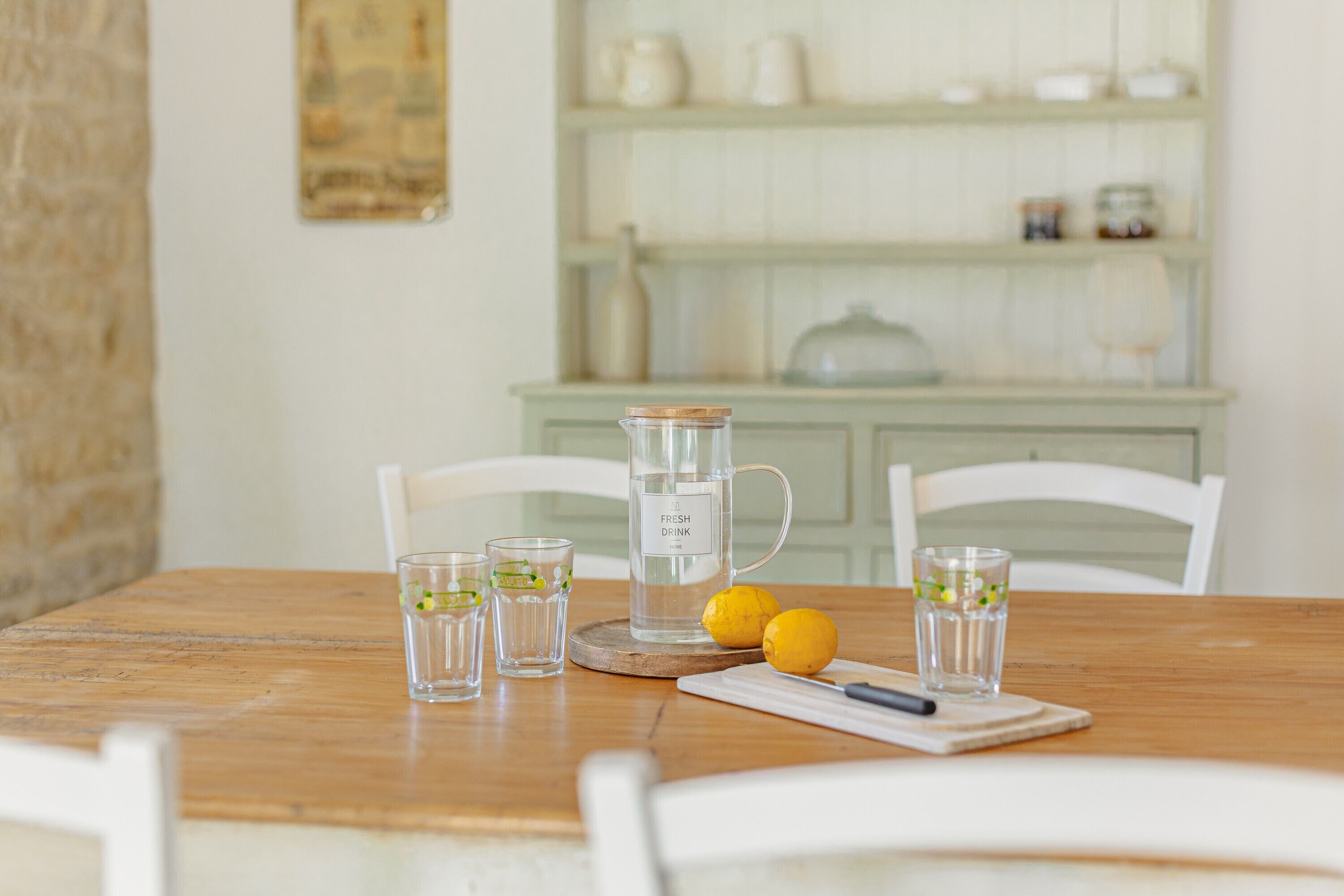 Une table en bois sur laquelle se trouvent une carafe, des verres, des citrons et un couteau posé sur une planche à découper.