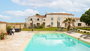 A swimming pool with lounge chairs, a patio area, and a large building with multiple windows and a tiled roof. - Maison 'Ambre' with Shared Pool & Spa, Private Terrace, and Wi-Fi (Vergné)