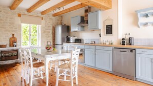 A kitchen with wooden beams, a dining table with chairs, a refrigerator, a microwave, and a dishwasher. - Maison 'Ambre' with Shared Pool & Spa, Private Terrace, and Wi-Fi (Vergné)