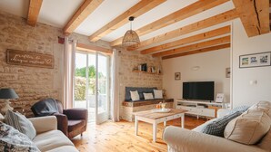 A cozy living room with a stone wall, wooden beams, a sofa, a coffee table, and a television. - Maison 'Ambre' with Shared Pool & Spa, Private Terrace, and Wi-Fi (Vergné)