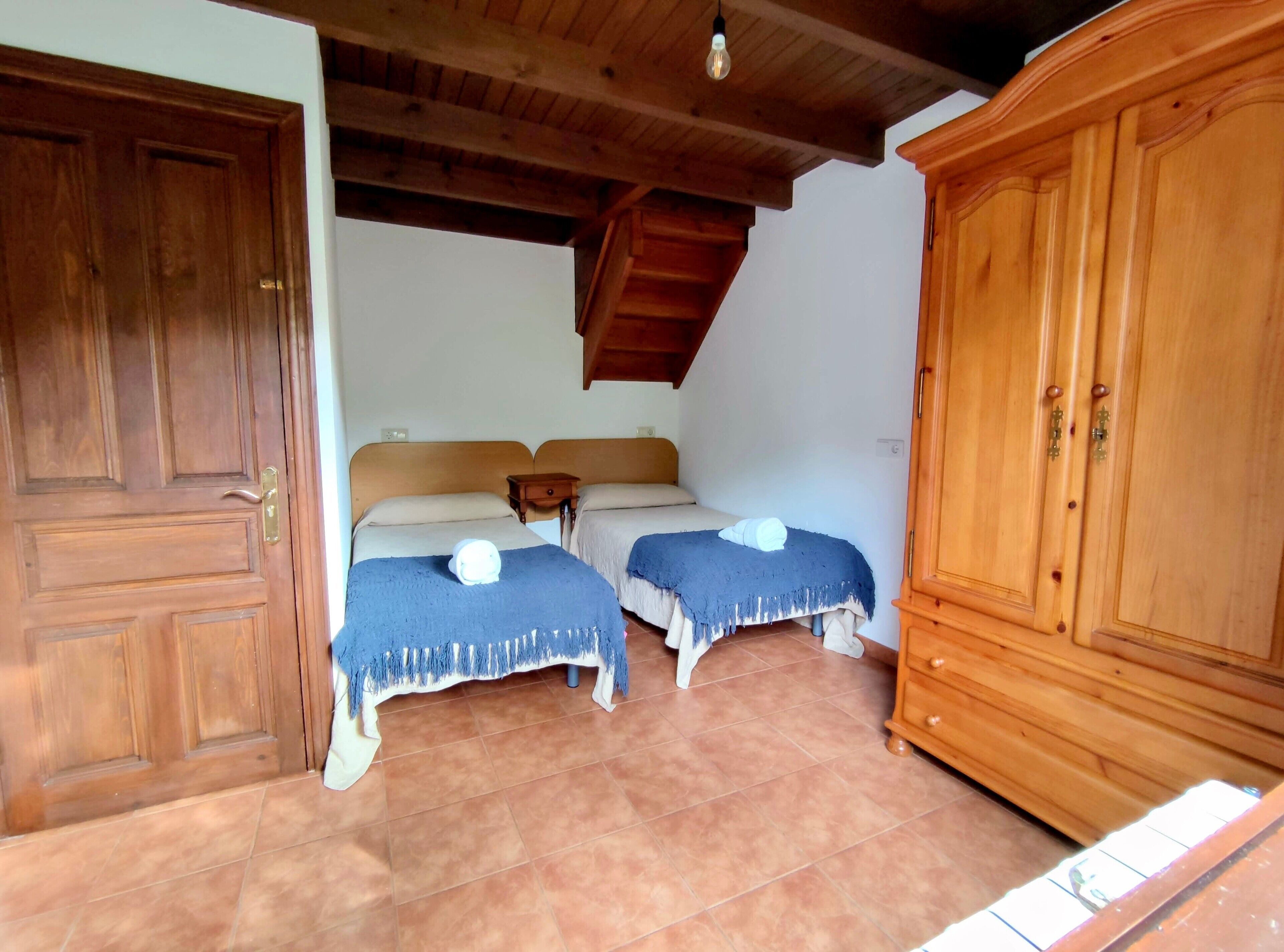 Une chambre avec deux lits, une armoire en bois et un sol carrelé.