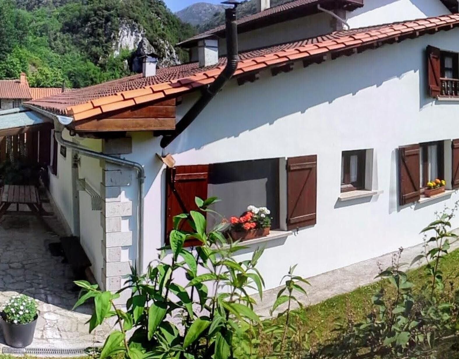 Une maison à deux étages, avec un toit recouvert de tuiles rouges, un escalier en pierre et un petit balcon agrémenté de plantes en pot.