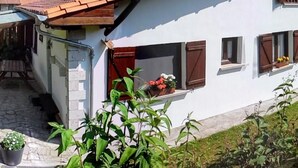 Una casa a due piani con tetto in tegole rosse, una scala in pietra e un piccolo balcone con piante in vaso.