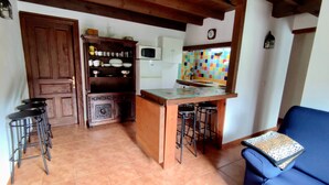 Una cucina con isola in legno, sgabelli da bar, un divano blu e pavimento piastrellato.