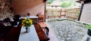 Eine Terrasse mit Tisch, Stühlen, einem Blumenstrauß, einer Ziegelwand, einem Holzzaun und Topfpflanzen.