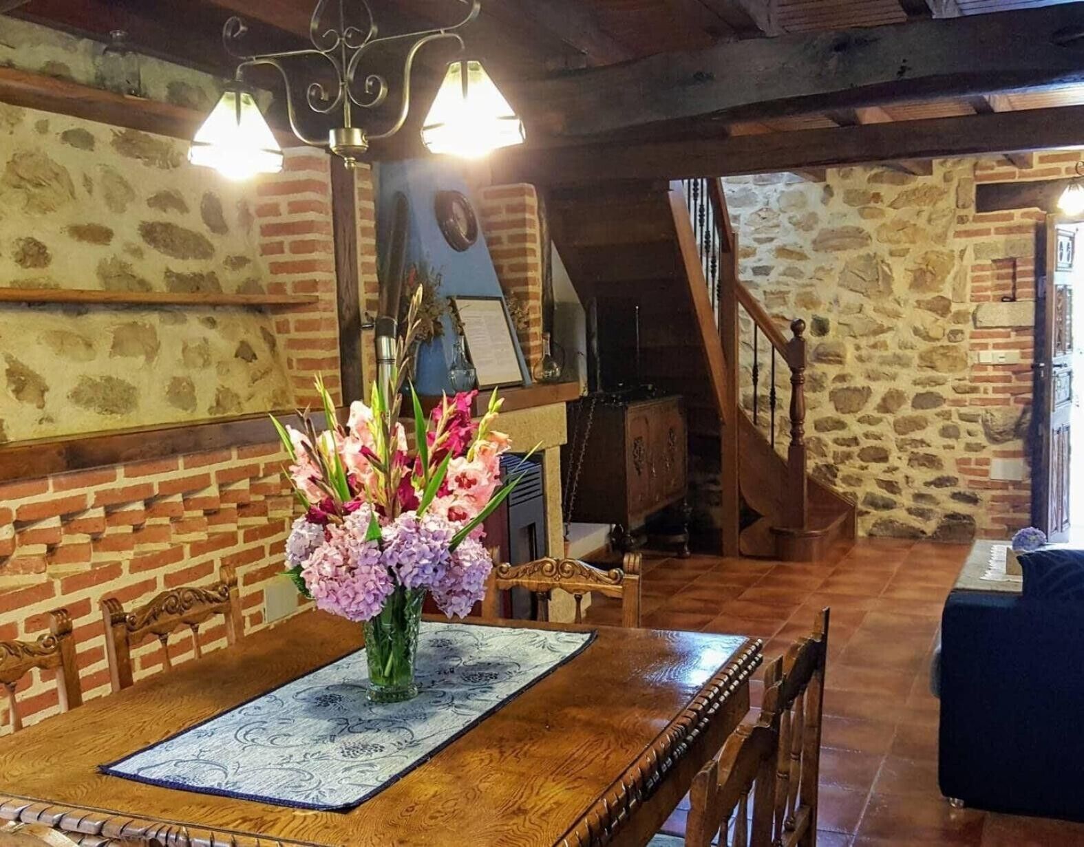 Een eetgedeelte met een houten tafel, stoelen, een bloemenvaas en een trap naar een andere kamer.