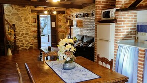 A rustic kitchen with a stone wall, wooden furniture, a dining table with a vase of flowers, and a microwave on top of a refrigerator. - ‘La Tablá’ Rural Apartment with Mountain Views, Private Terrace, and Wi-Fi (Alles)
