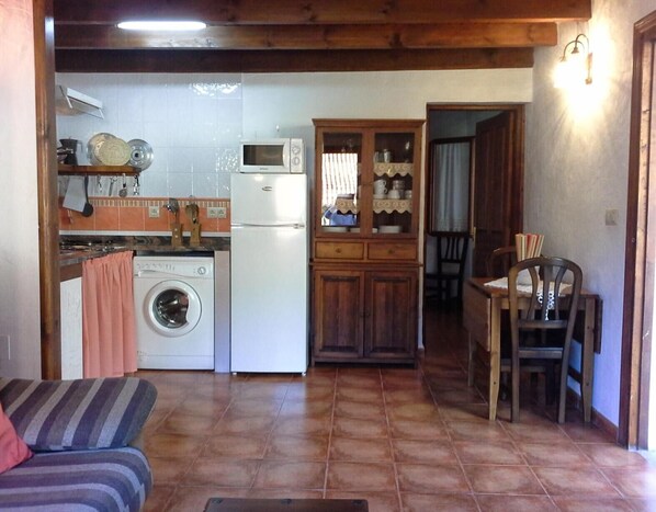 A compact kitchen with a washing machine, microwave, and wooden cabinets.