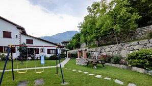 A grassy backyard with a swing set, a stone wall, and a stone building with a chimney. - Apartment 'Jana' with Mountain View, Private Terrace and Wi-Fi (Alles)