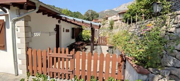 Un bâtiment rustique doté d’un portail en bois, d’un mur en pierre et d’un petit jardin fleuri.