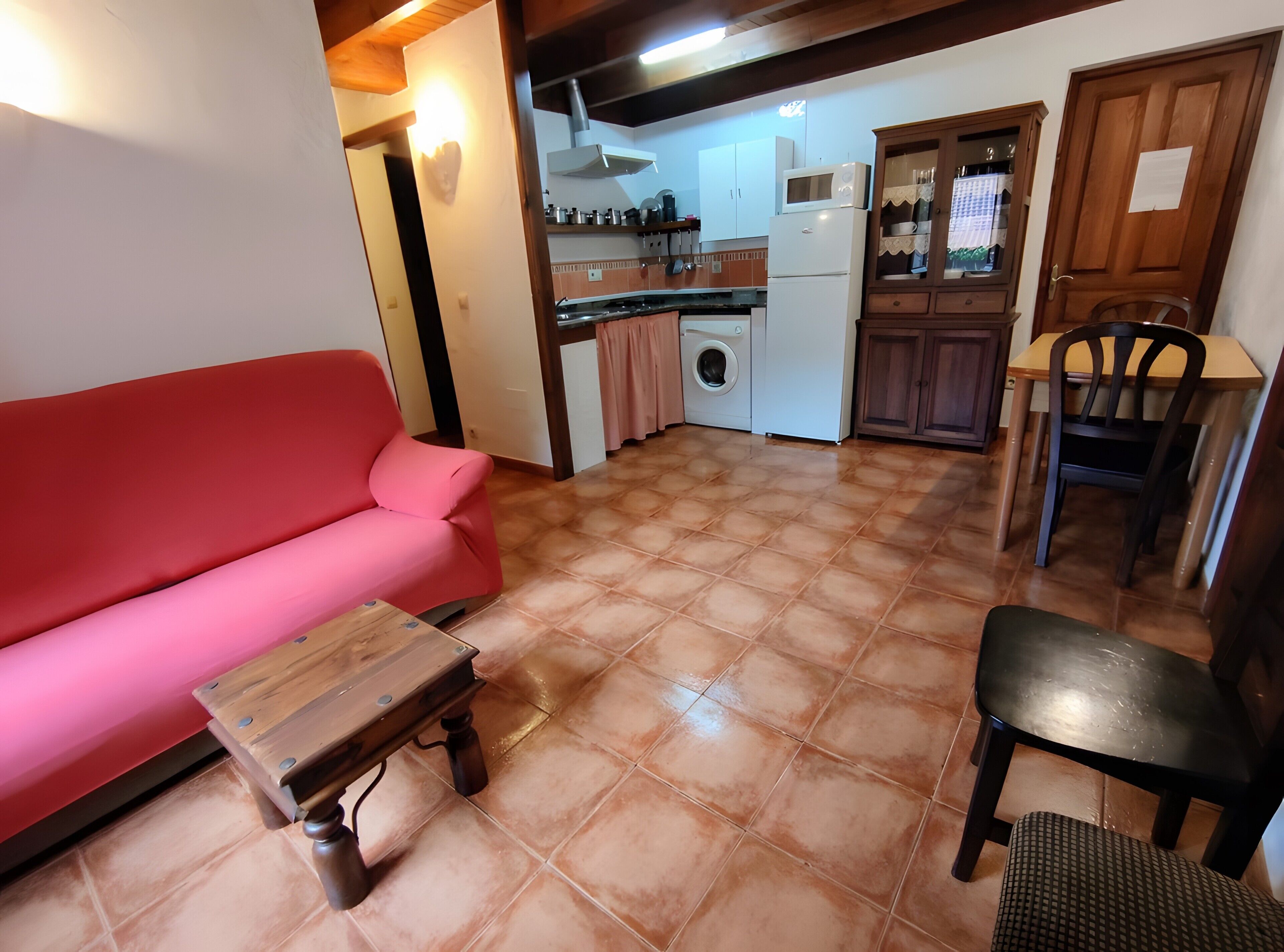 A living area with a sofa, a small wooden table, a chair, and a kitchen in the background.